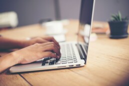 Close-up woman hands typing on laptop in office.