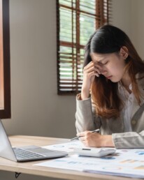 Upset woman touching head using calculator and laptop for calculating finance. Frustration young