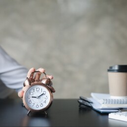 A person's hand presses the desk clock to turn off the alarm.